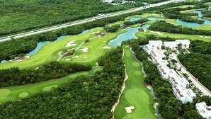 An aerial view of a golf course with multiple bunkers and water hazards, surrounded by dense greenery and a large resort building with multiple units. - Akumal Seaside Ocean View | Beach Access 11 Pools (Akumal)
