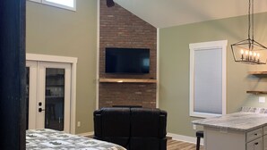 A spacious living area with a large bed, a fireplace, a ceiling fan, and a kitchen island. - Charming studio in beautiful Hendersonville with AC, WiFi, hot tub & gated (Hendersonville)