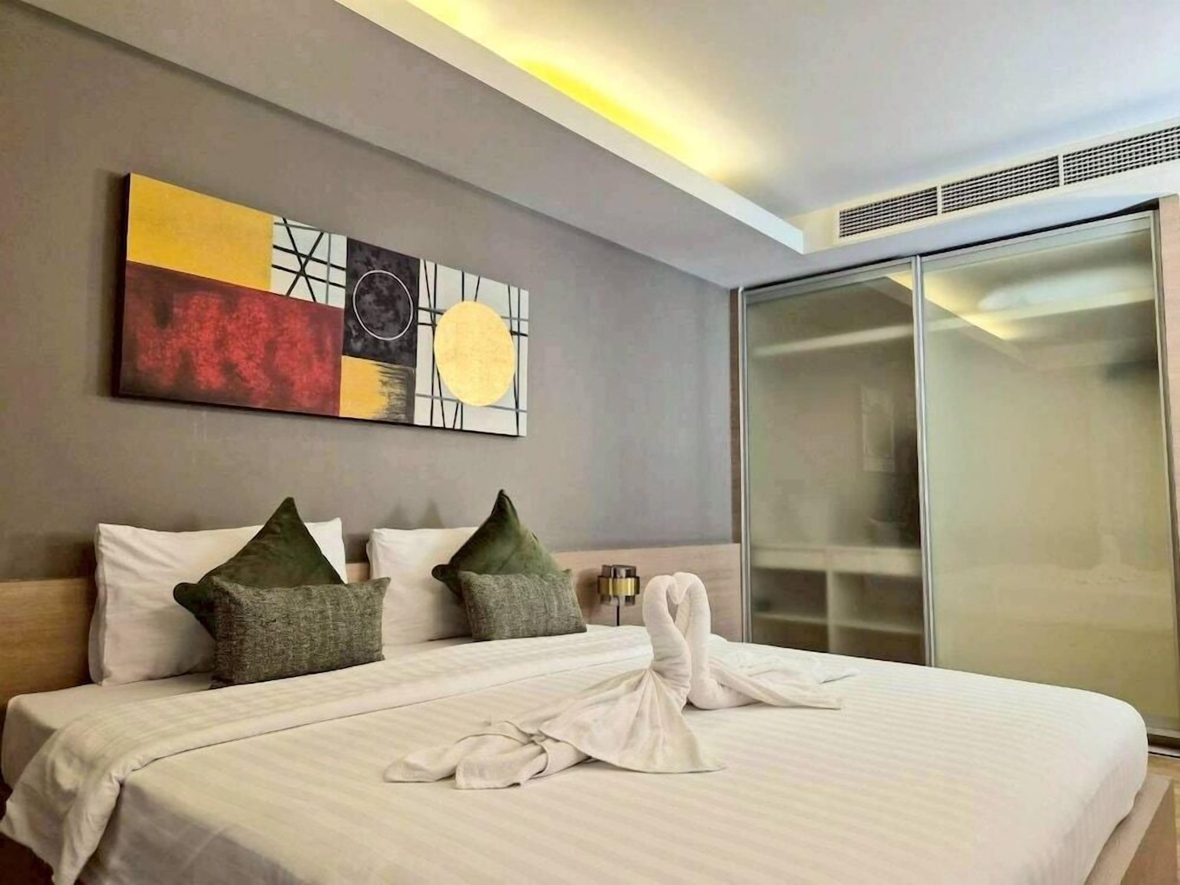 A hotel room with a bed, pillows, a robe, and a painting on the wall.