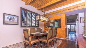 A dining area with a wooden table and chairs, a patterned rug, and a hanging light fixture.