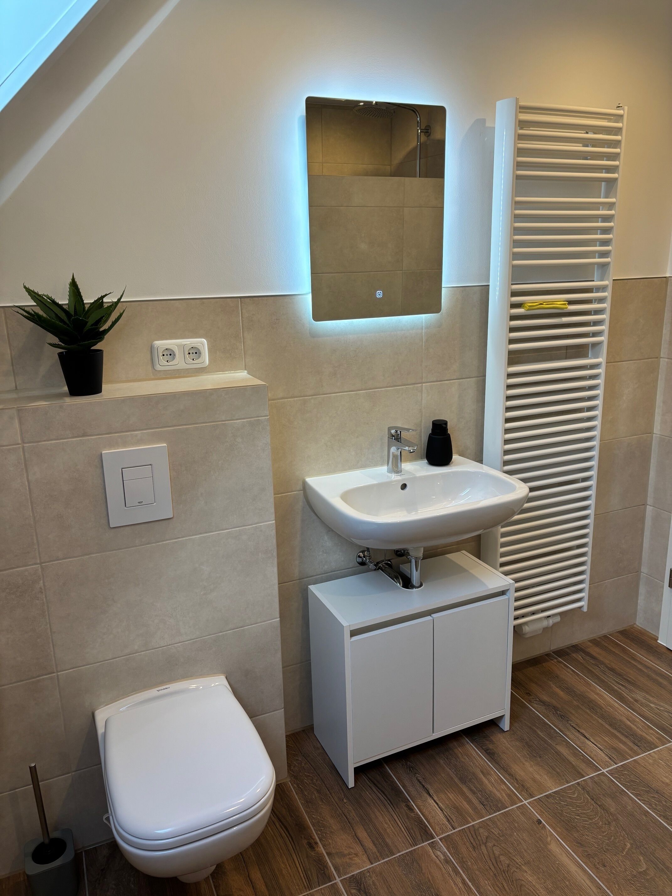 A modern bathroom with a white sink, a toilet, a mirror, and a radiator.