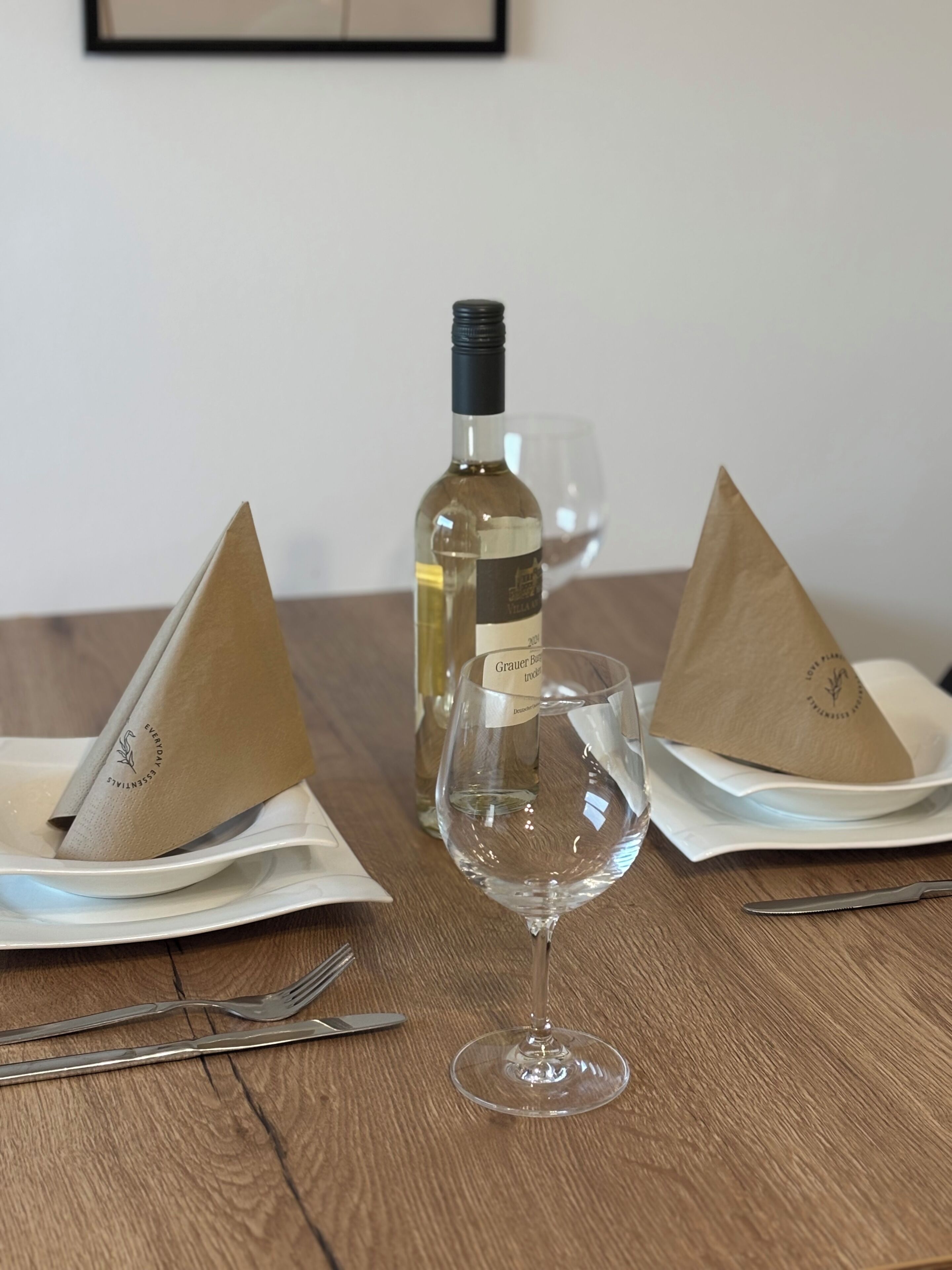 Una mesa con una botella de vino, dos servilletas dobladas, una copa de vino y cubiertos.