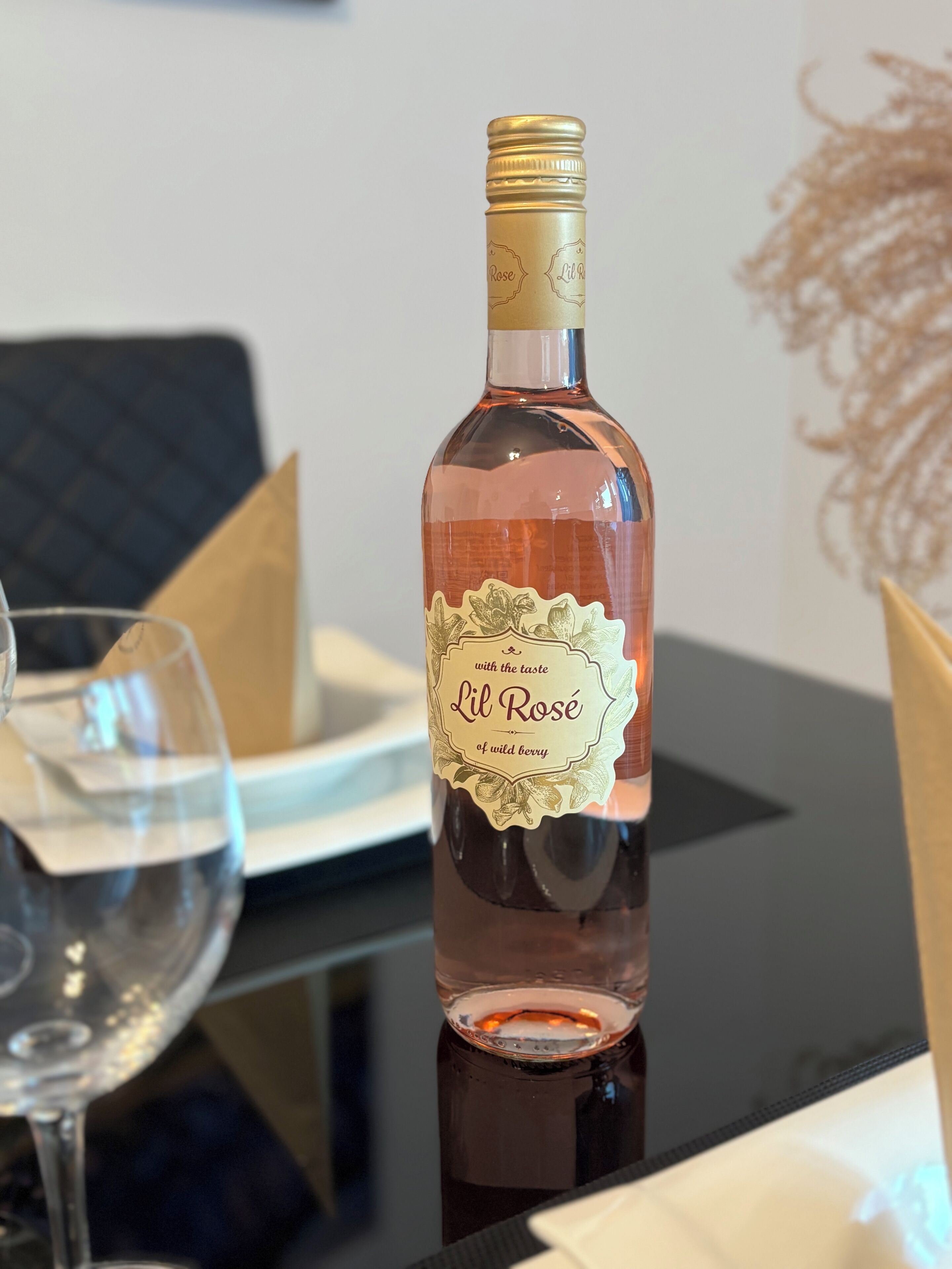 A bottle of Lil Rose wine on a table with a glass and a napkin.