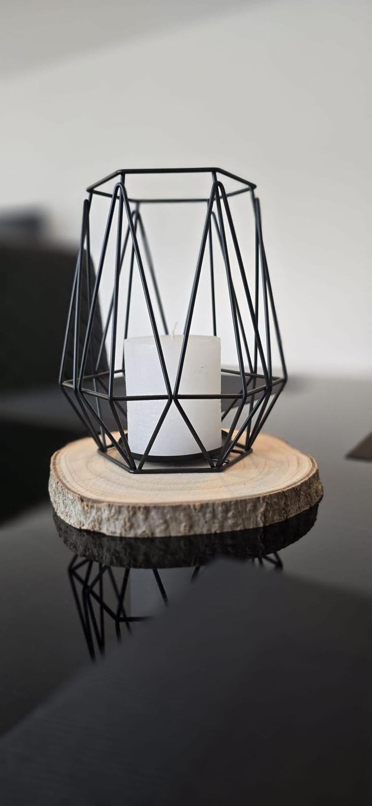 Ein geometrischer Kerzenständer mit einem würfelförmigen Teelicht auf einem Holzuntersetzer.