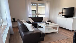 A modern living room with a black leather sofa, a white coffee table, and a television on a white cabinet. - Quiet time out in Soltau (Soltau)