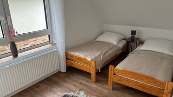 Un dormitorio con dos camas de madera, un radiador, una ventana que da a un muro de ladrillo y una pequeña mesa con una lámpara.