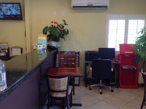 A reception area with a counter, chairs, a computer desk, an air conditioner, and a potted plant. - Garden Inn San Gabriel (Temple City)