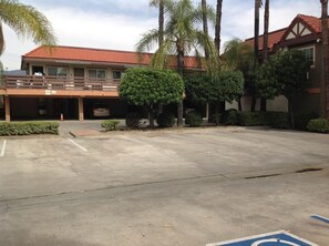 A parking lot with a building that has a red-tiled roof and a balcony. - Garden Inn San Gabriel (Temple City)