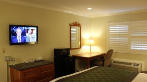 A hotel room with a bed, a desk with a lamp, a television, a mirror, and a heater. - Garden Inn San Gabriel (Temple City)