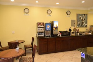 Un vestíbulo de hotel con un mostrador de recepción, relojes mostrando la hora de Pekín, Los Ángeles y Nueva York, una máquina de caf é y un cuadro en la pared.