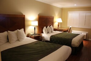 Habitación de hotel con dos camas, lámparas de noche, mesitas de noche, un escritorio y una ventana con persianas.