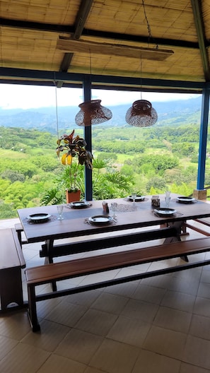 A dining table set with plates, glasses, and a pitcher, overlooking a lush green landscape. - La María Nature Reserve – Infinity Pool, Mountain Views, and Horses (Armenia)