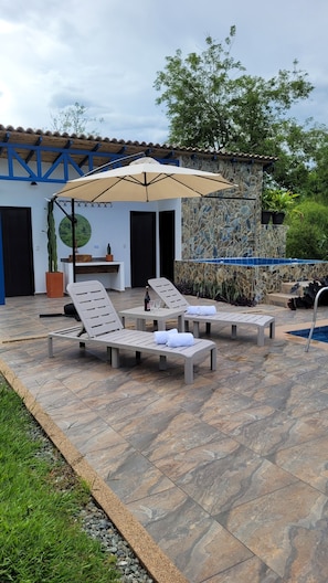 An outdoor seating area with lounge chairs and a table, a stone wall with a mosaic design, and a potted plant.