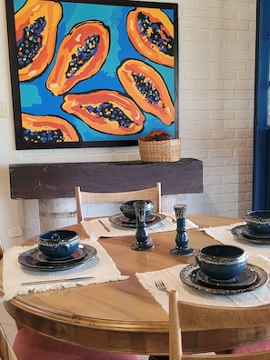 Una mesa de comedor con vajilla azul y negra, un cuenco decorativo y un cuadro de papaya en la pared de arriba.