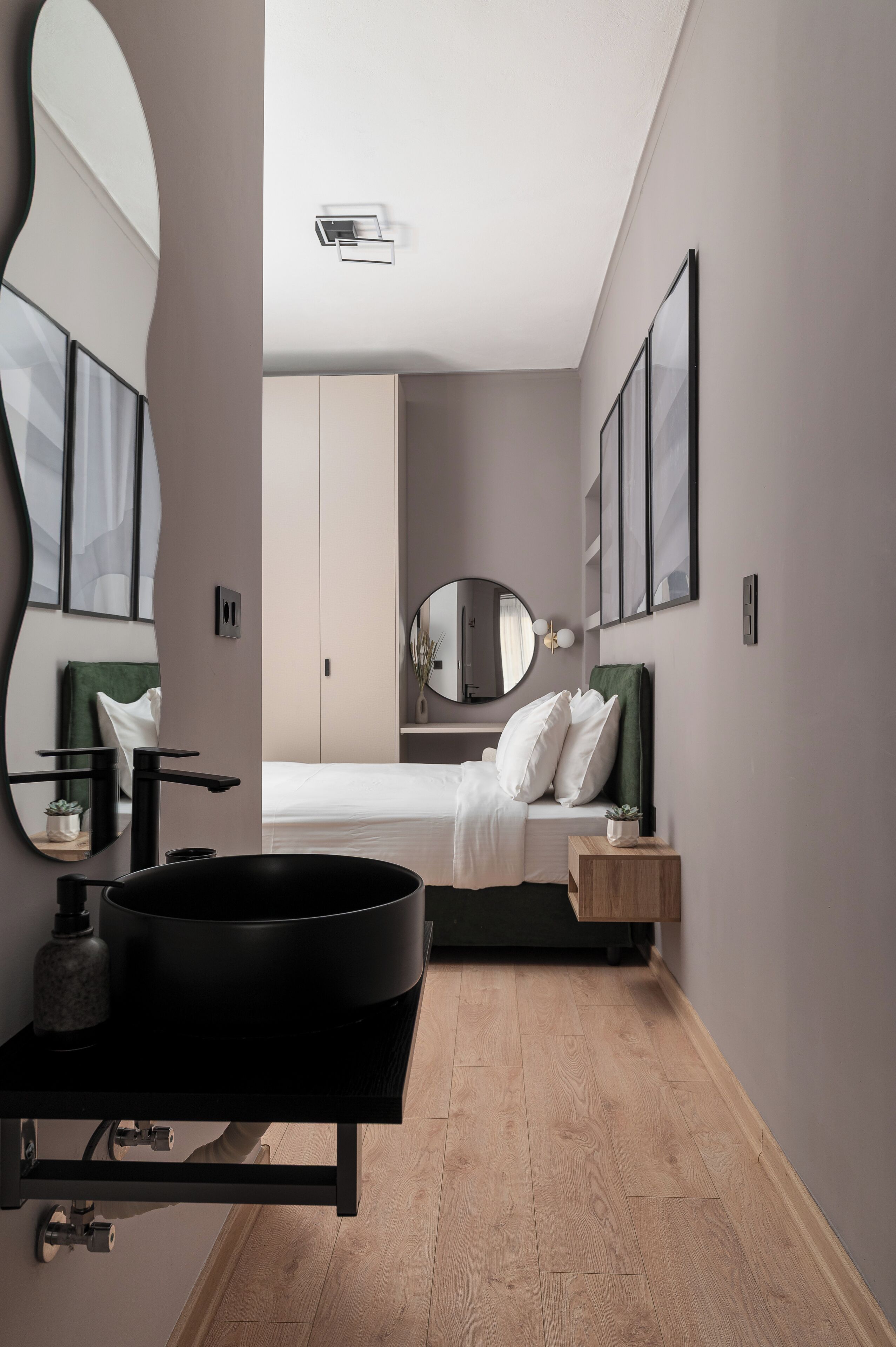 A modern bedroom with a large mirror, a round black sink, a bed with white linens, and a green headboard.