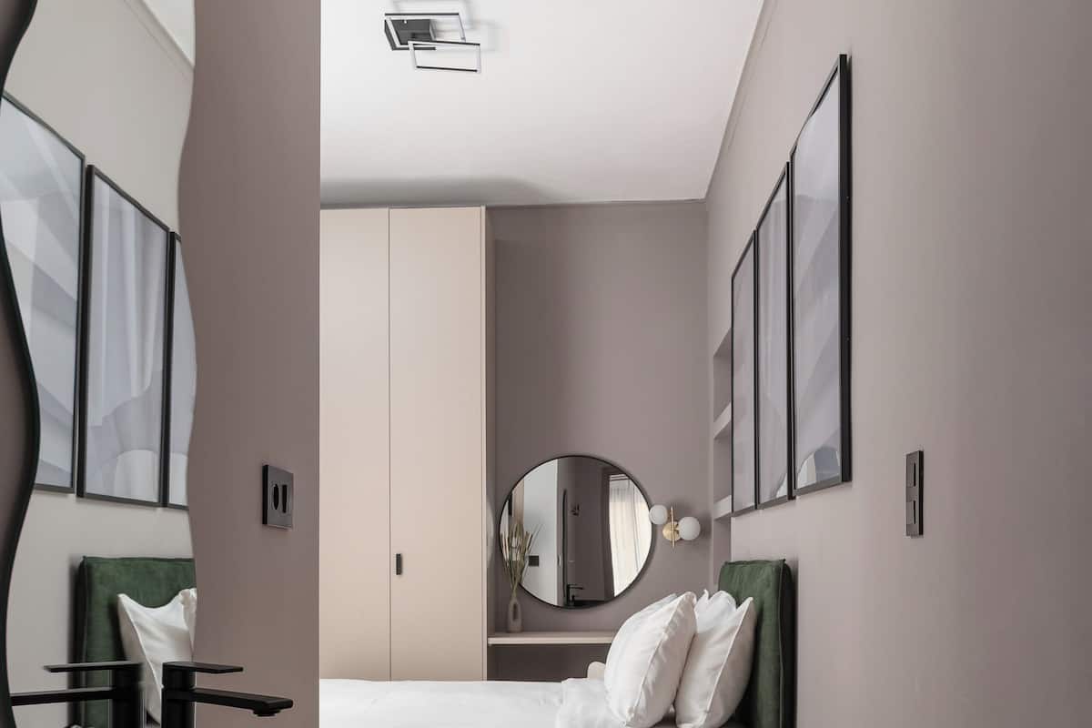 A modern bedroom with a large mirror, a round black sink, a bed with white bedding, and a green headboard.