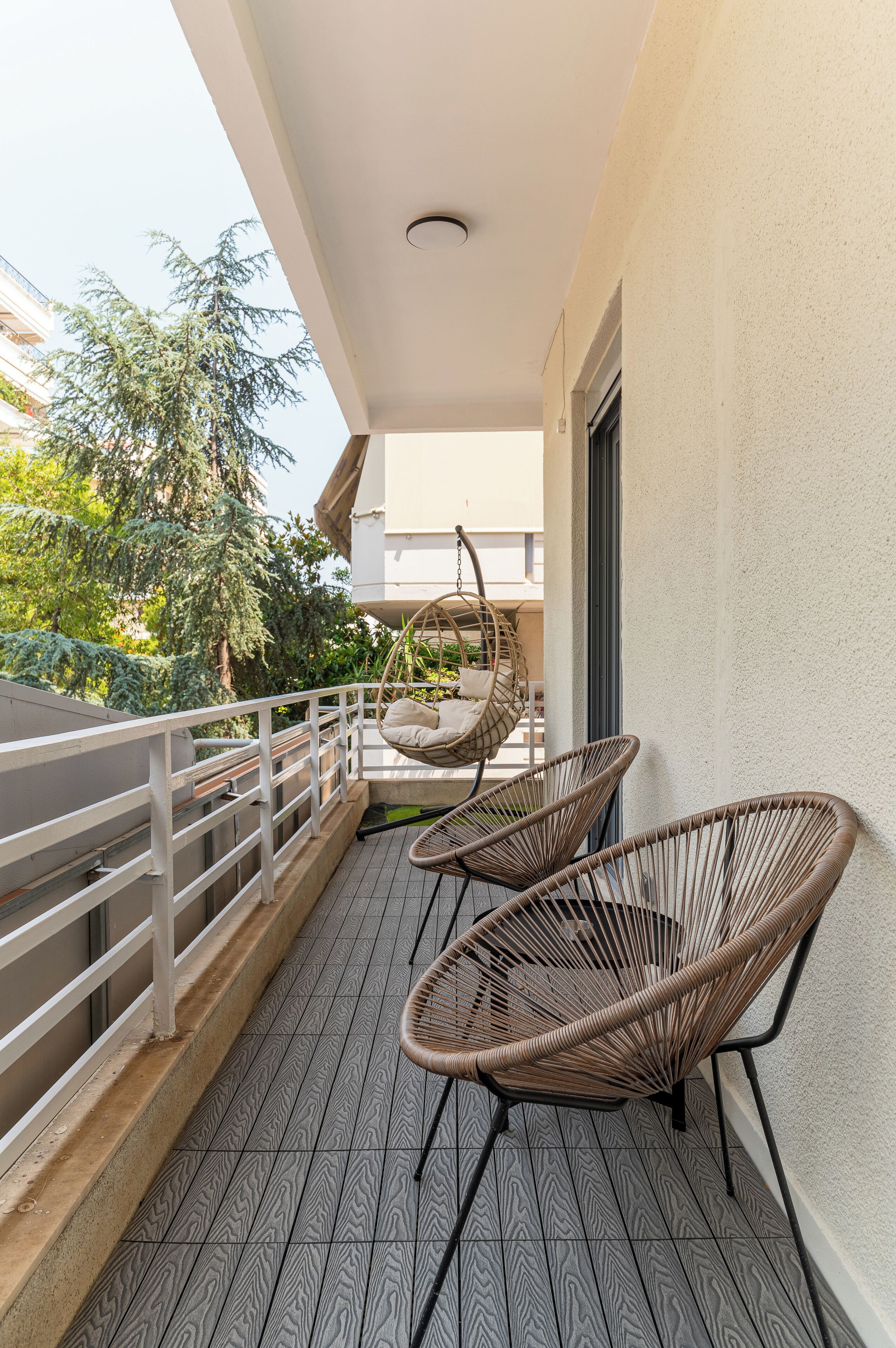 A balcony with wicker chairs, a hanging chair, and a view of greenery.
