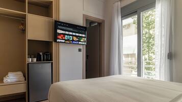 Ein Hotelzimmer mit einem Bett, einem an der Wand befestigten Fernseher, der einen Streaming-Dienst zeigt, einer kleinen Kühlbox und einem Kleiderschrank mit darin befindlichen Kleidungsstücken.