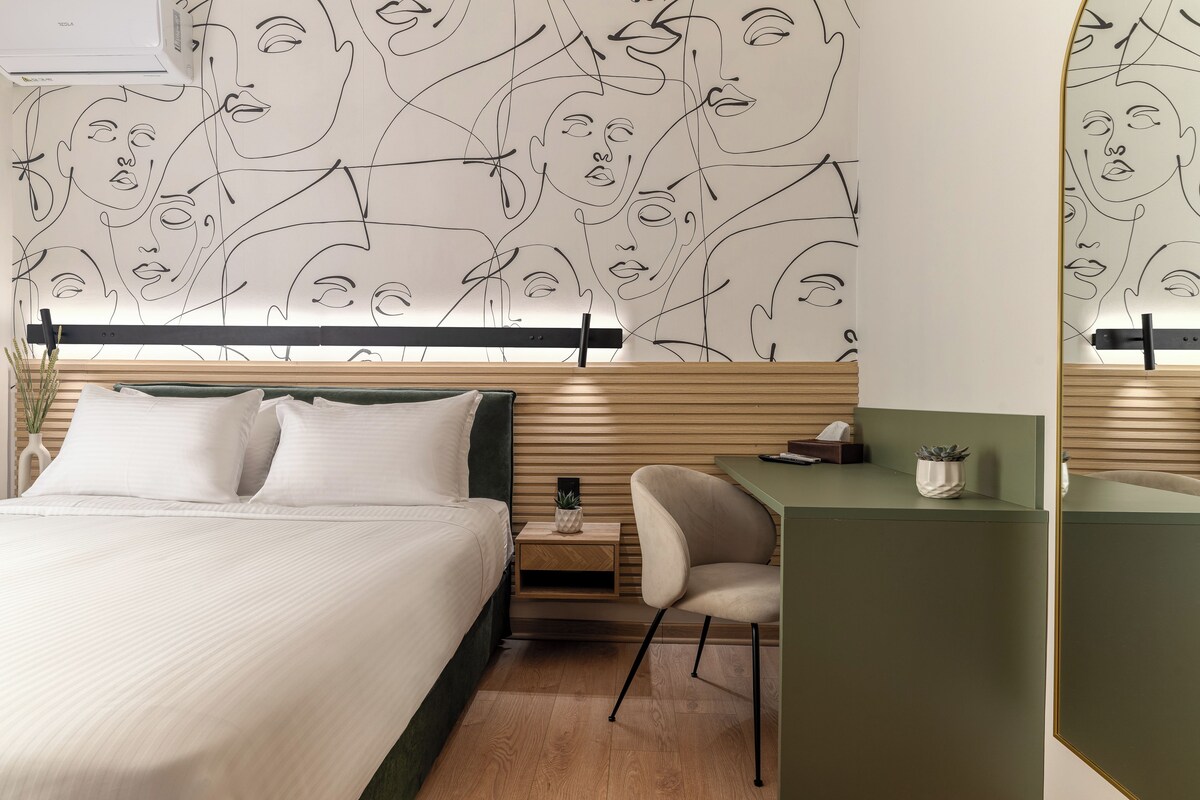 Ett modernt hotellrum med en säng, ett skrivbord och en vägg prydd med abstrakt linjekonst.