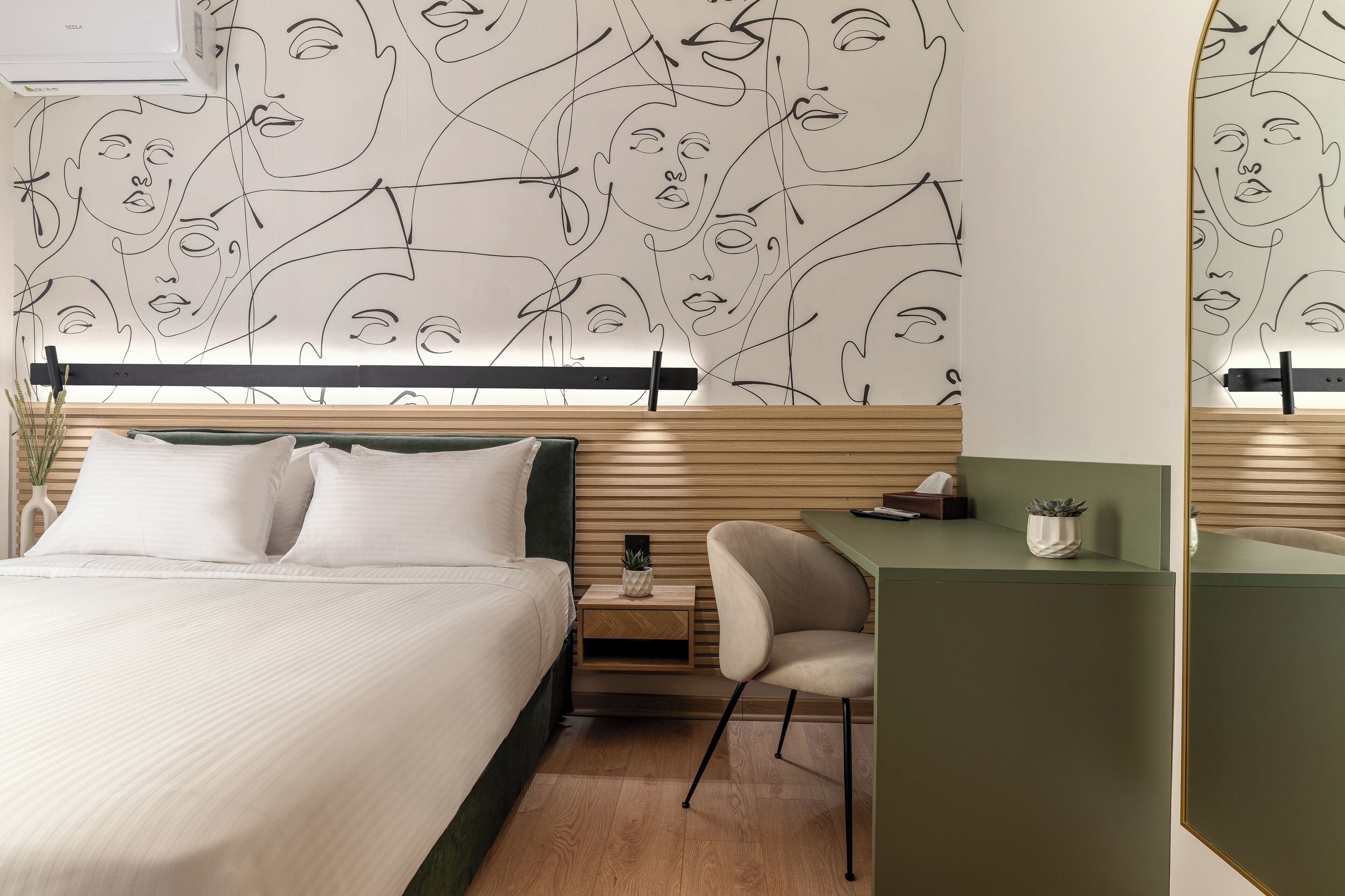 A modern hotel room with a bed, a desk, and a wall with abstract line art.