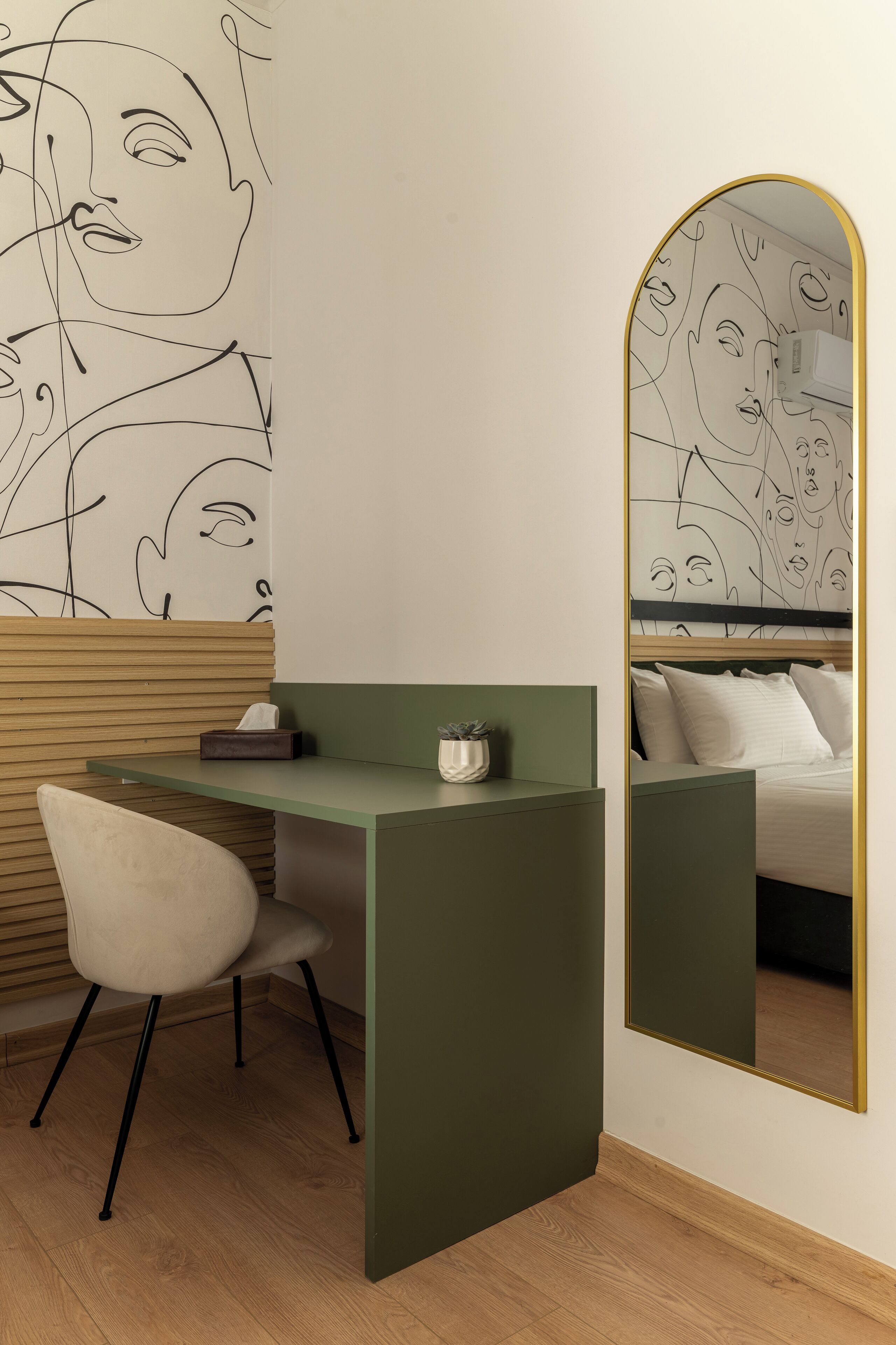 Ein modernes Zimmer mit einem grünen Schreibtisch, einem weißen Stuhl, einem großen Spiegel und einer Wand mit abstrakter Linienkunst.