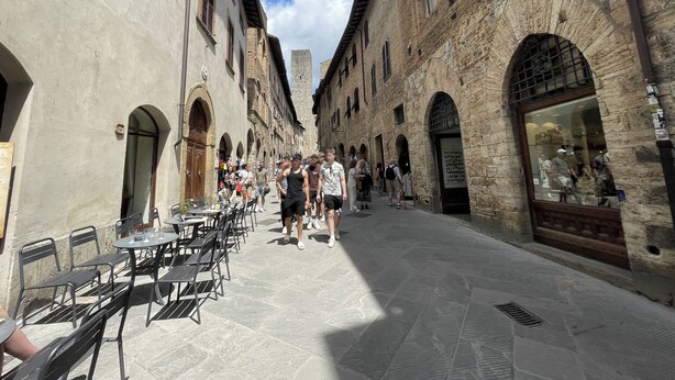 A narrow street lined with stone buildings, outdoor seating, and a few people walking. - La Casa di Ines (San Gimignano)