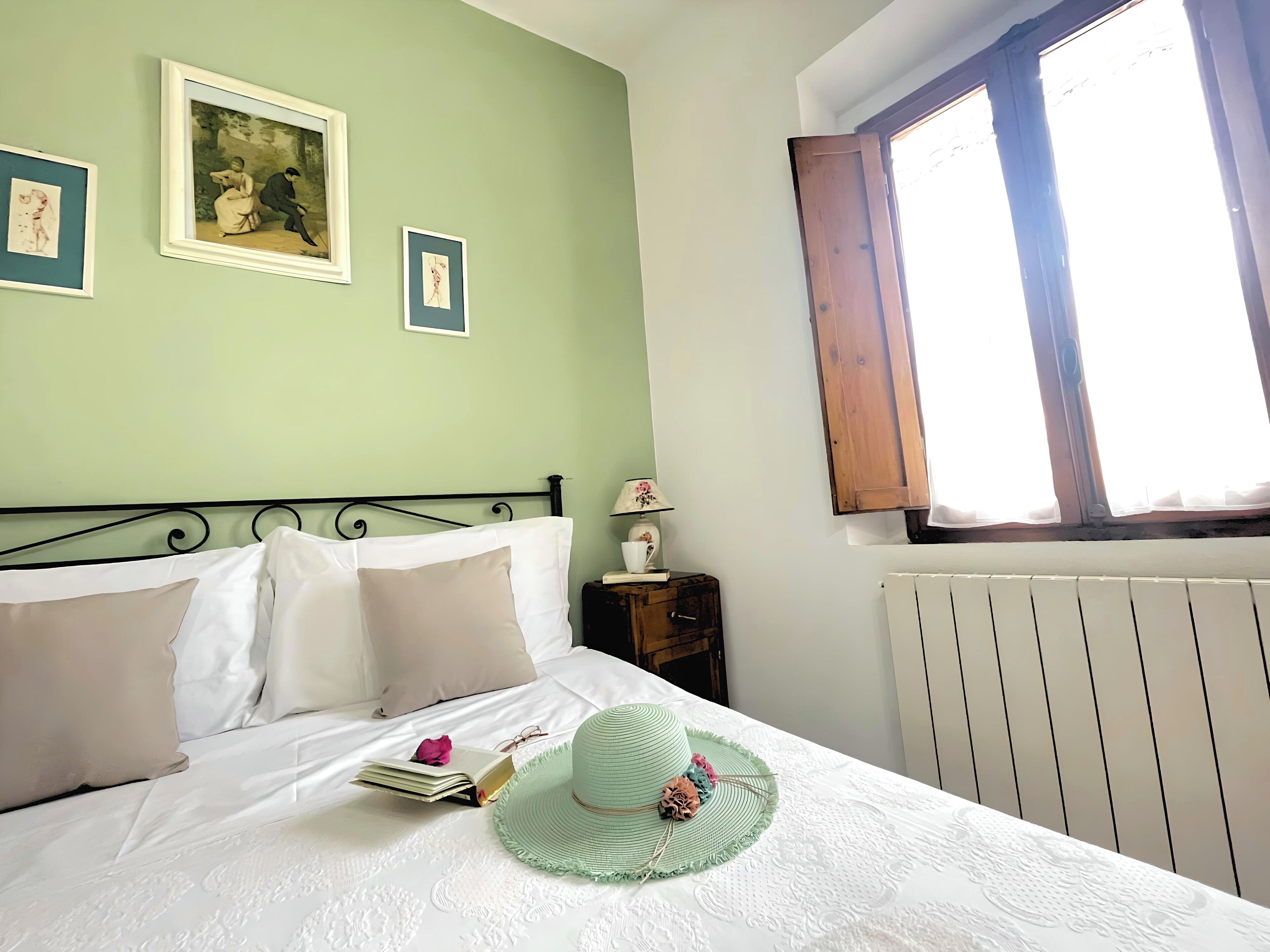Une chambre à coucher avec un lit, des oreillers, un chapeau, un livre et une lampe sur une table de chevet.