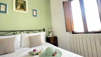 Une chambre à coucher avec un lit, des oreillers, un chapeau, un livre et une lampe sur une table de chevet.