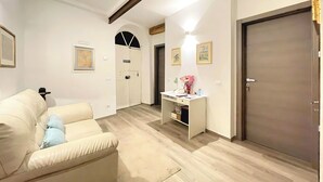 A modern living room with a beige sofa, a desk with a vase of flowers, and a closed door. - La Casa di Ines (San Gimignano)