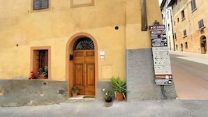 A yellow building with a wooden double door, potted plants, and a signboard with directional information. - La Casa di Ines (San Gimignano)