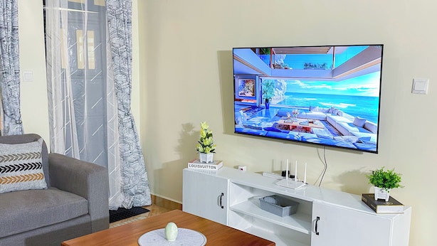 A living room with a sofa, a coffee table, a TV mounted on the wall, and a white cabinet.