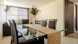 Un coin repas avec une table en verre, des chaises foncées, un chemin de table en tissu tissé et un vase rempli de fleurs.