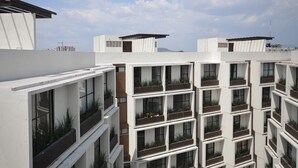 Un immeuble moderne à plusieurs étages, doté de balcons, chacun agrémenté de jardinières contenant des plantes.