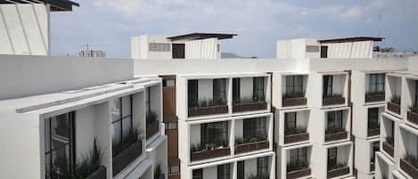 A modern multi-story building with balconies, each with a planter box containing plants.