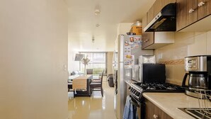 Une cuisine moderne équipée d’une cuisinière, d’un four et d’un réfrigérateur. On aperçoit à l’arrière-plan un coin repas avec une table et des chaises.