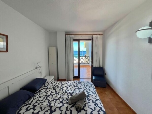 Habitación de hotel con cama, armario, escritorio y vista a la playa desde la puerta.