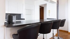 A modern kitchen with white cabinets, a black countertop, and a bar area with four black bar stools.