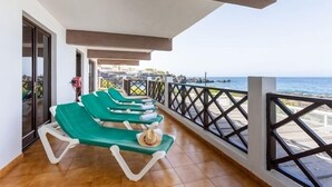 A balcony with green lounge chairs and a view of the sea.