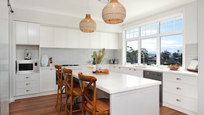 Een moderne keuken met witte kastjes, een groot kookeiland, houten stoelen en uitzicht door de ramen.