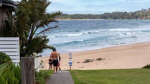 Une plage avec une promenade en bois menant au rivage, un panneau indiquant les règles à respecter sur la plage, et une vue sur l’océan et les bâtiments situés au loin.