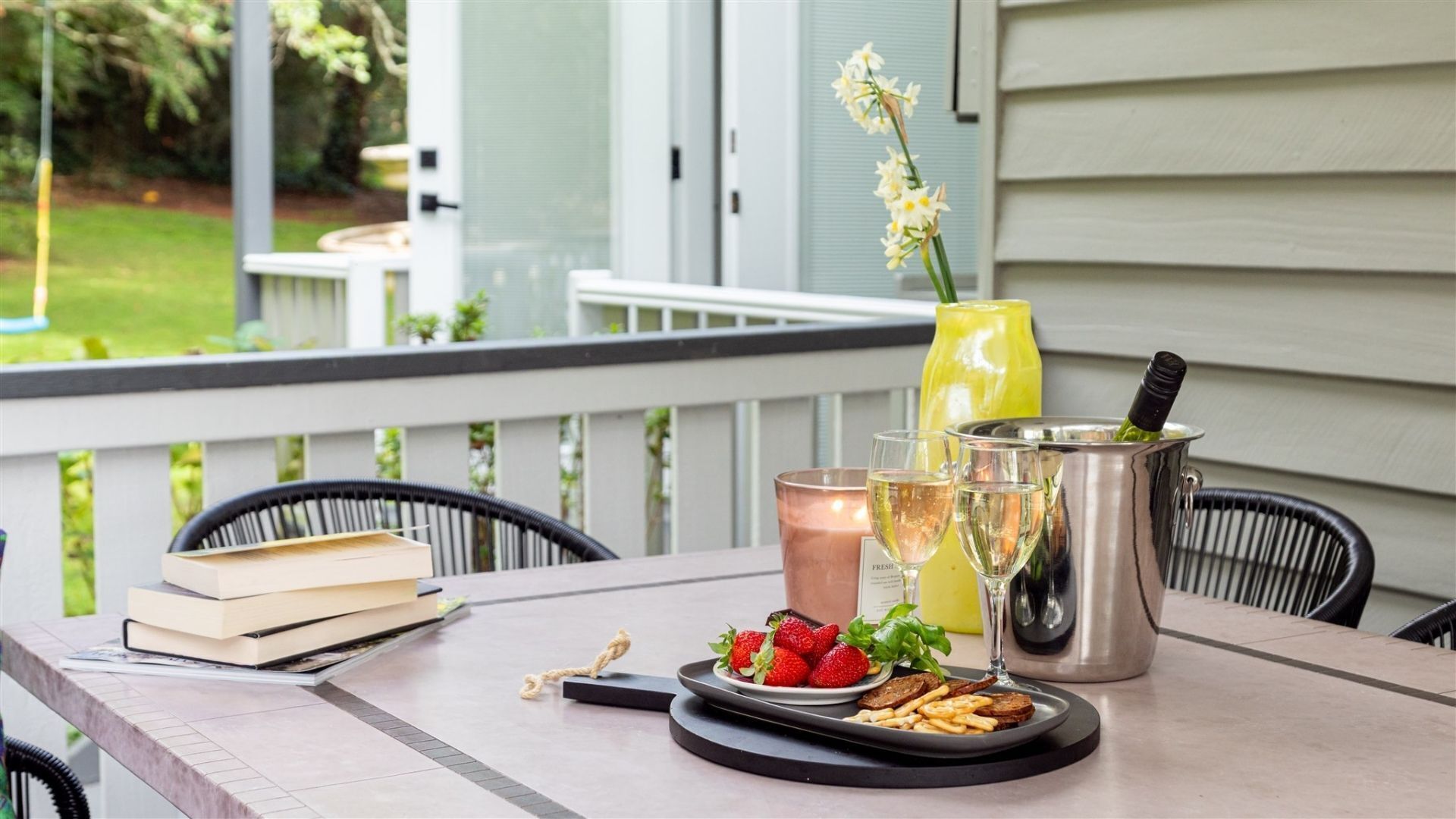 A patio table with a book, a plate of strawberries, a candle, and a drink pitcher.