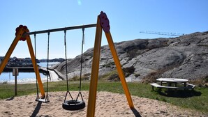 A swing set with a tire swing, a picnic table, and a rocky landscape with a body of water and a crane in the background. - Newly renovated apartment in Skärhamn within walking distance to the beach | SE09138 (Skärhamn)