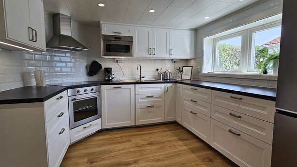 A modern kitchen with white cabinetry, a built-in oven, a microwave, and a window with a view of greenery outside. - Newly renovated apartment in Skärhamn within walking distance to the beach | SE09138 (Skärhamn)