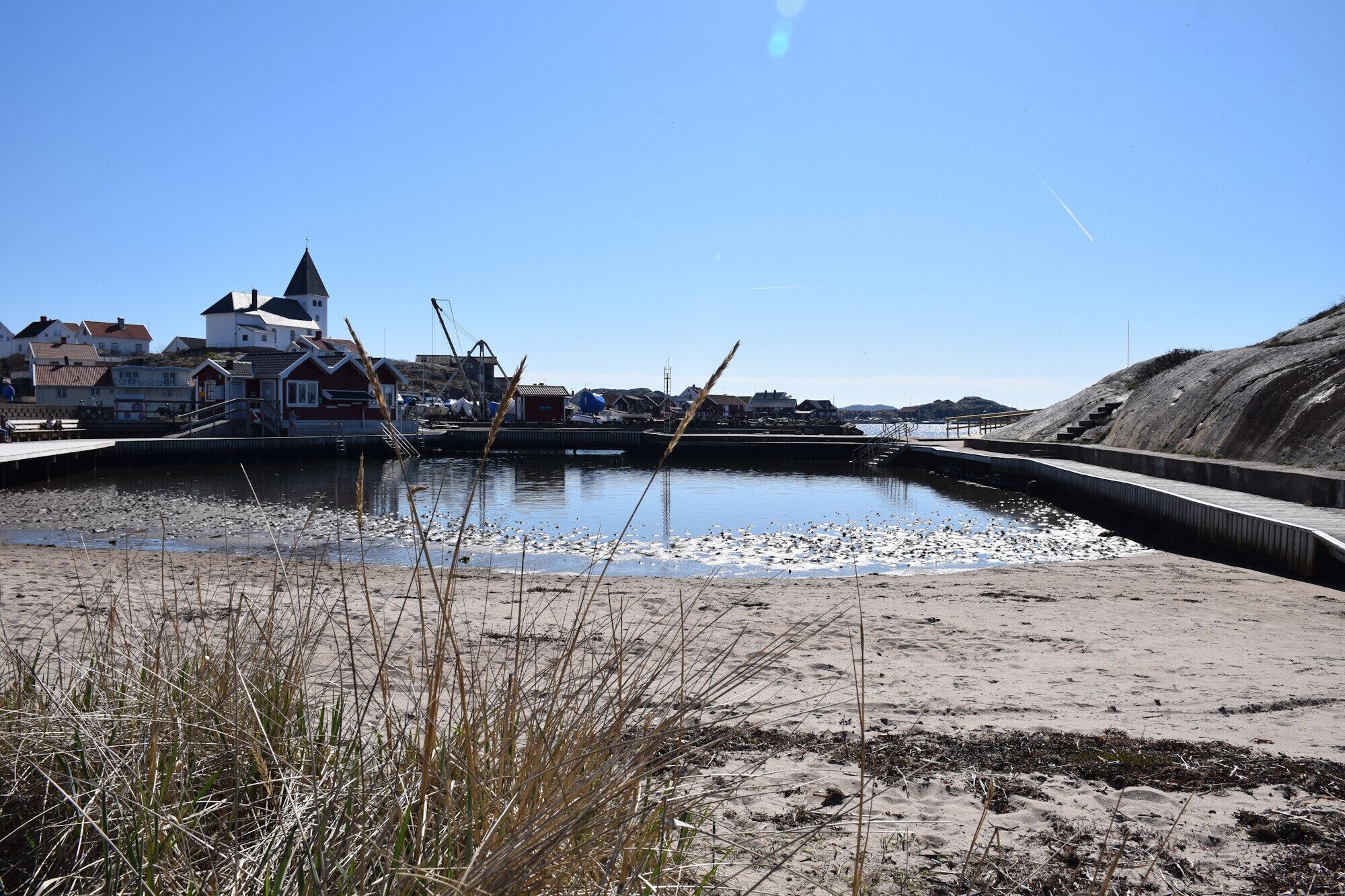 A coastal area with a sandy beach, a small water body, and buildings in the background.
