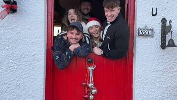 Een groep mensen staat bij een rode deur met een bord waarop 'Merry Christmas' staat.