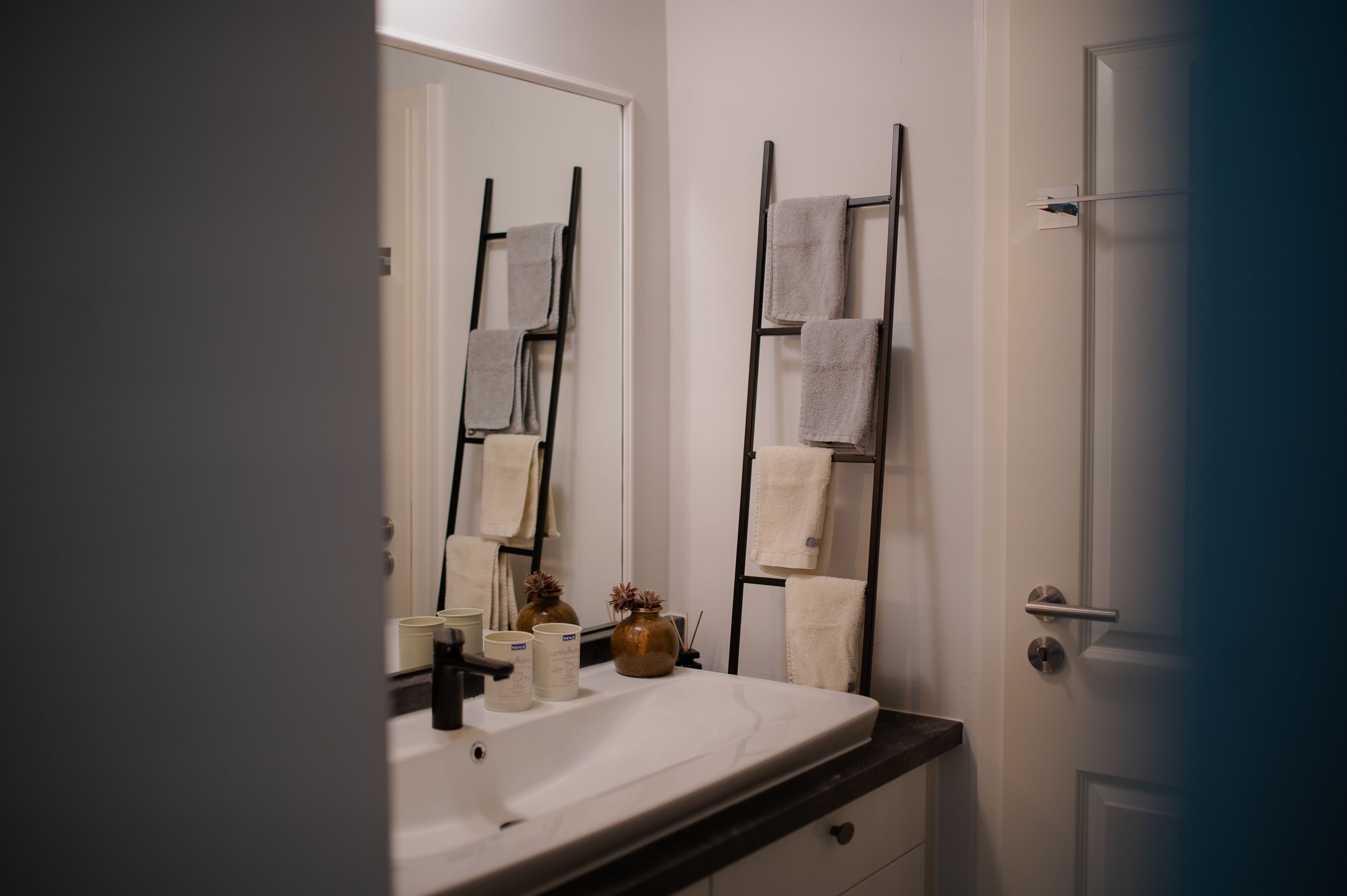 Un baño con lavamanos blanco, un espejo y dos barras para toallas.