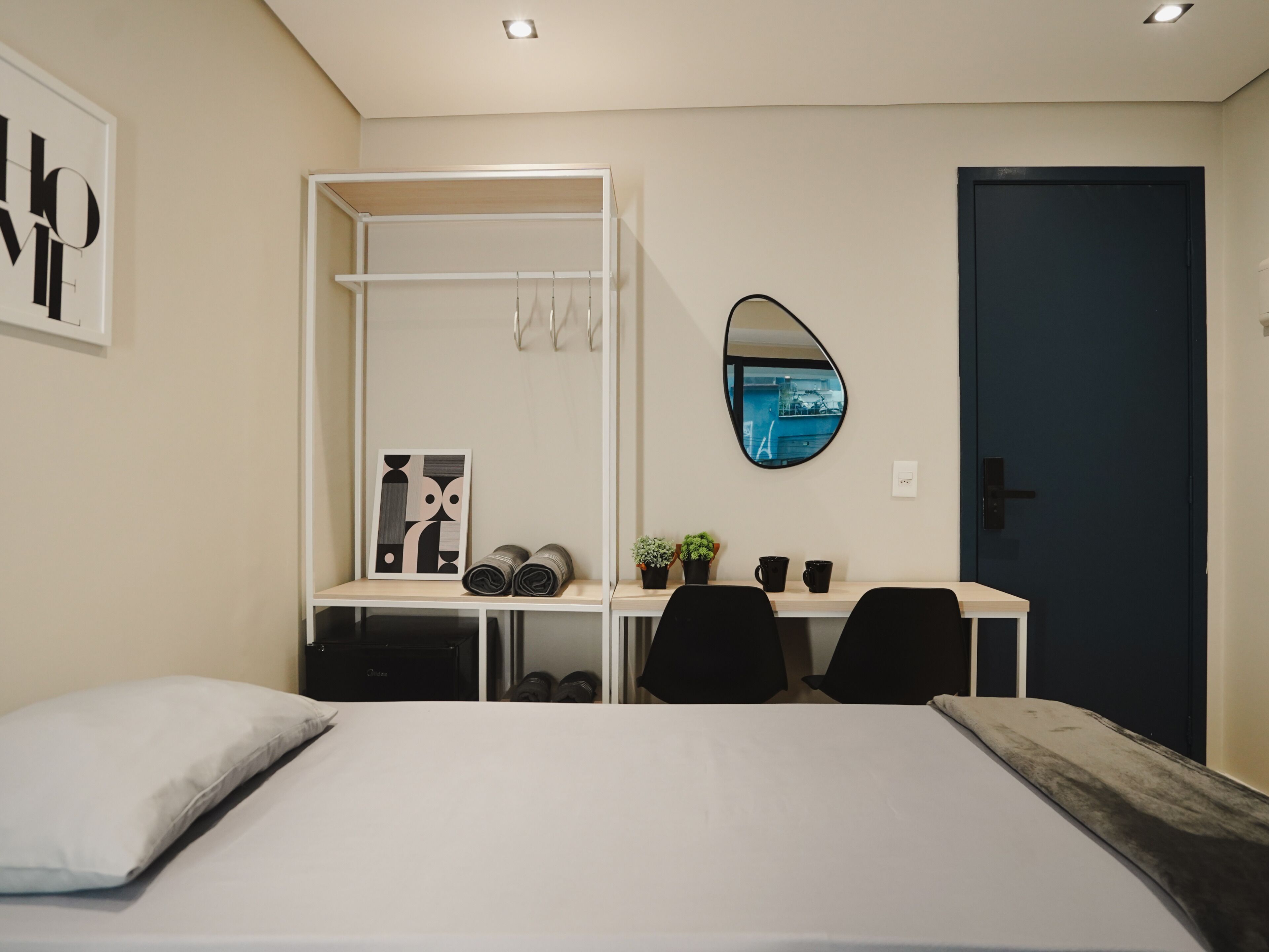 Een slaapkamer met een bed, een bureau en een stoel. Er is een kledingkast, een spiegel en een deur.