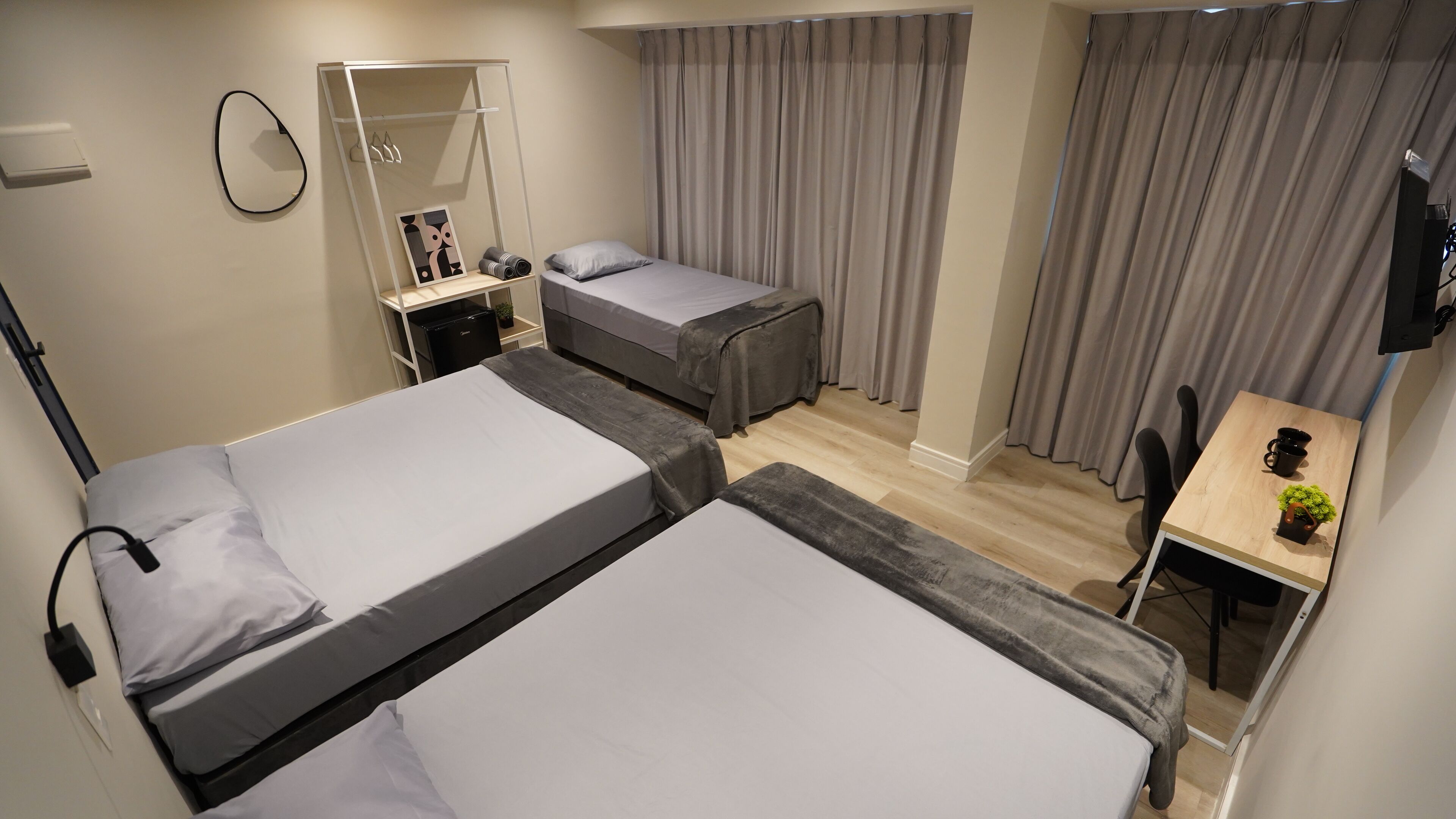 A hotel room with two beds, a desk, a chair, a TV, and a wardrobe.
