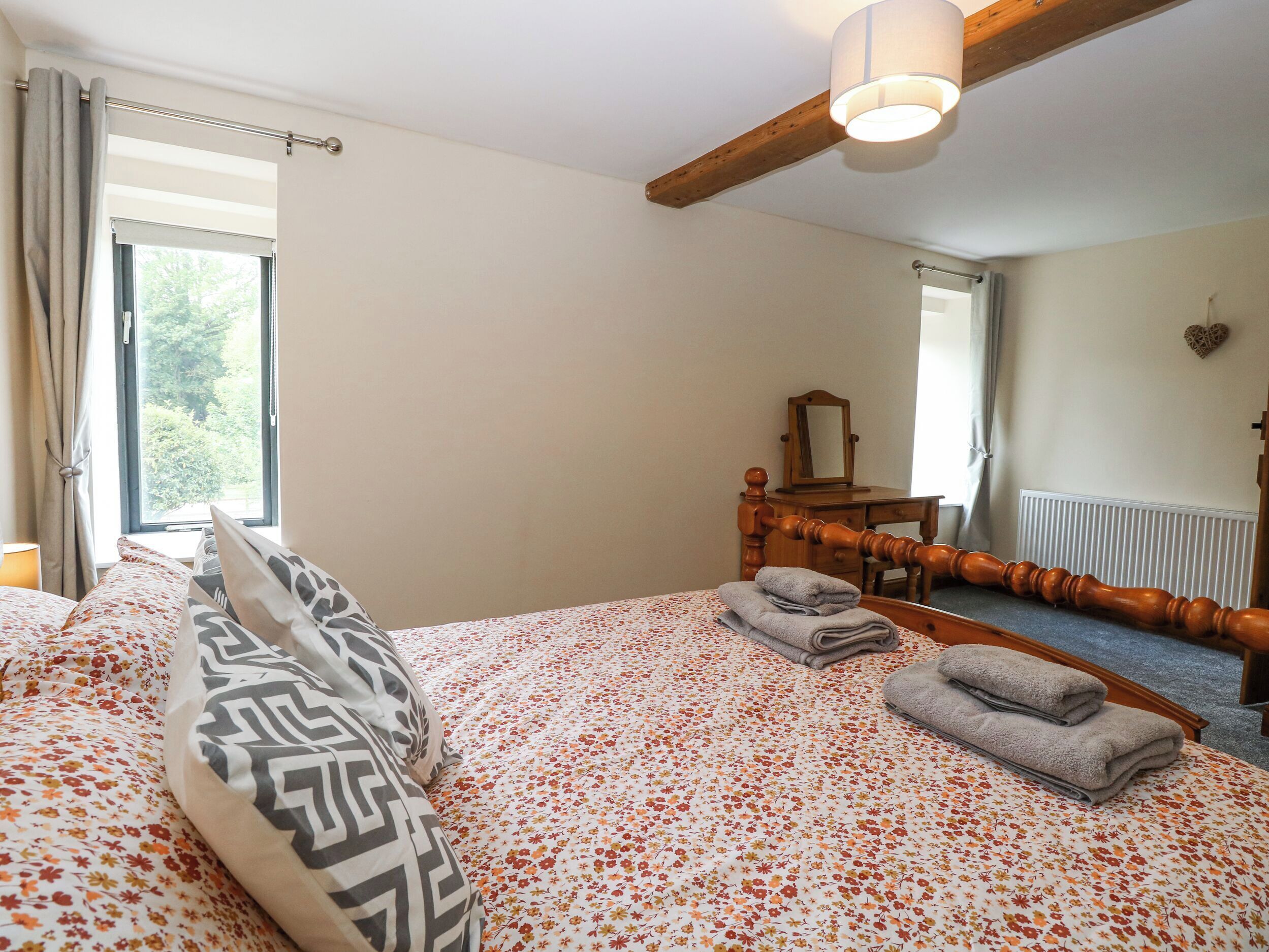 A bedroom with a bed, a dresser, a mirror, and a window with curtains.