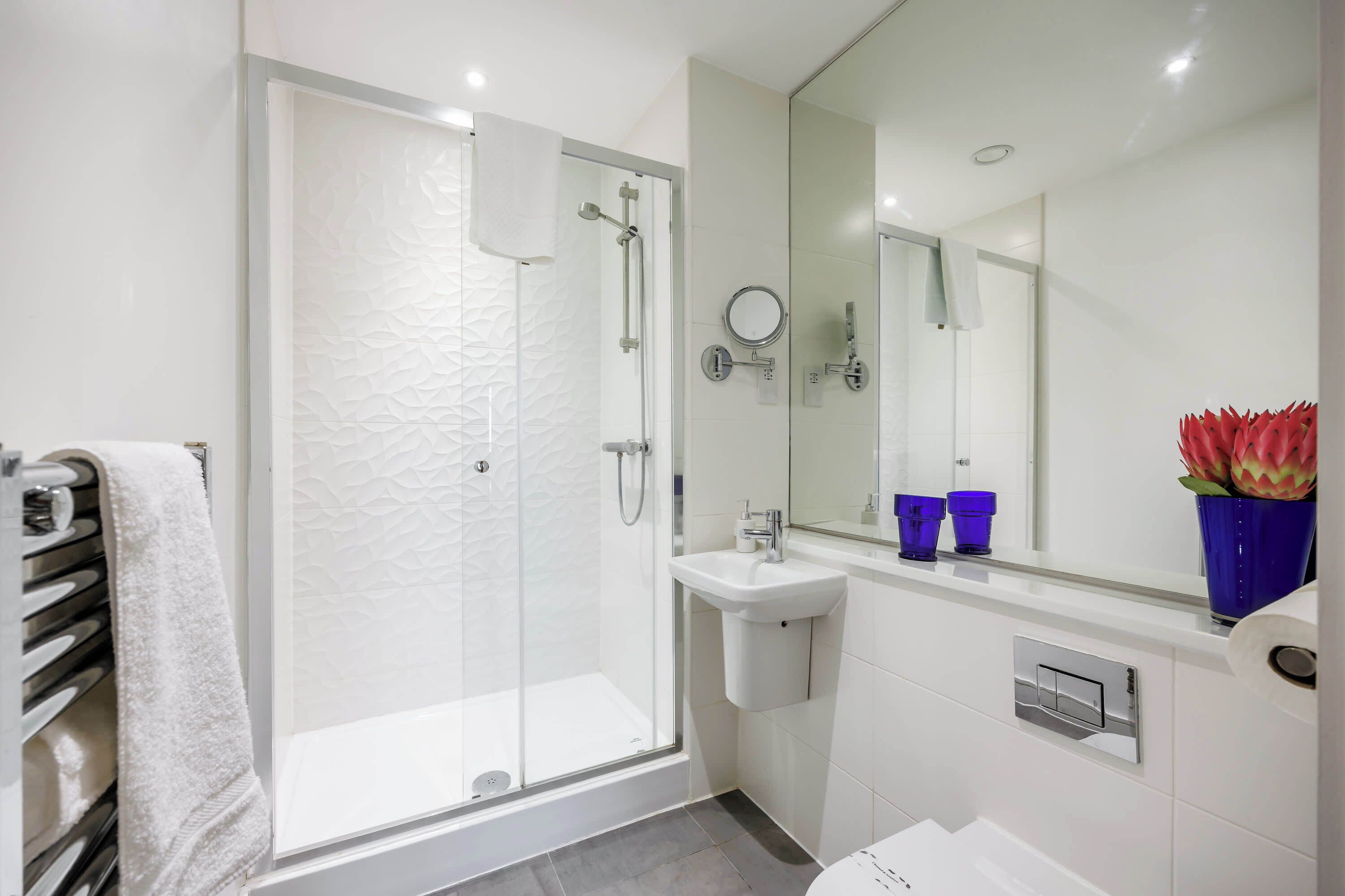 A modern bathroom with a glass-enclosed shower, a white sink, and a large mirror.
